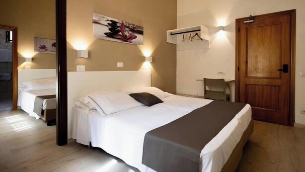 A hotel room with a large bed, a desk, a chair, and a wooden door. - Hotel Miralaghi Family & Sport (Chianciano Terme)