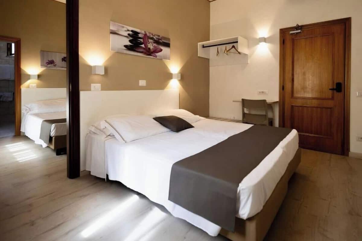 Quarto de hotel com cama grande, escrivaninha, cadeira e porta de madeira.