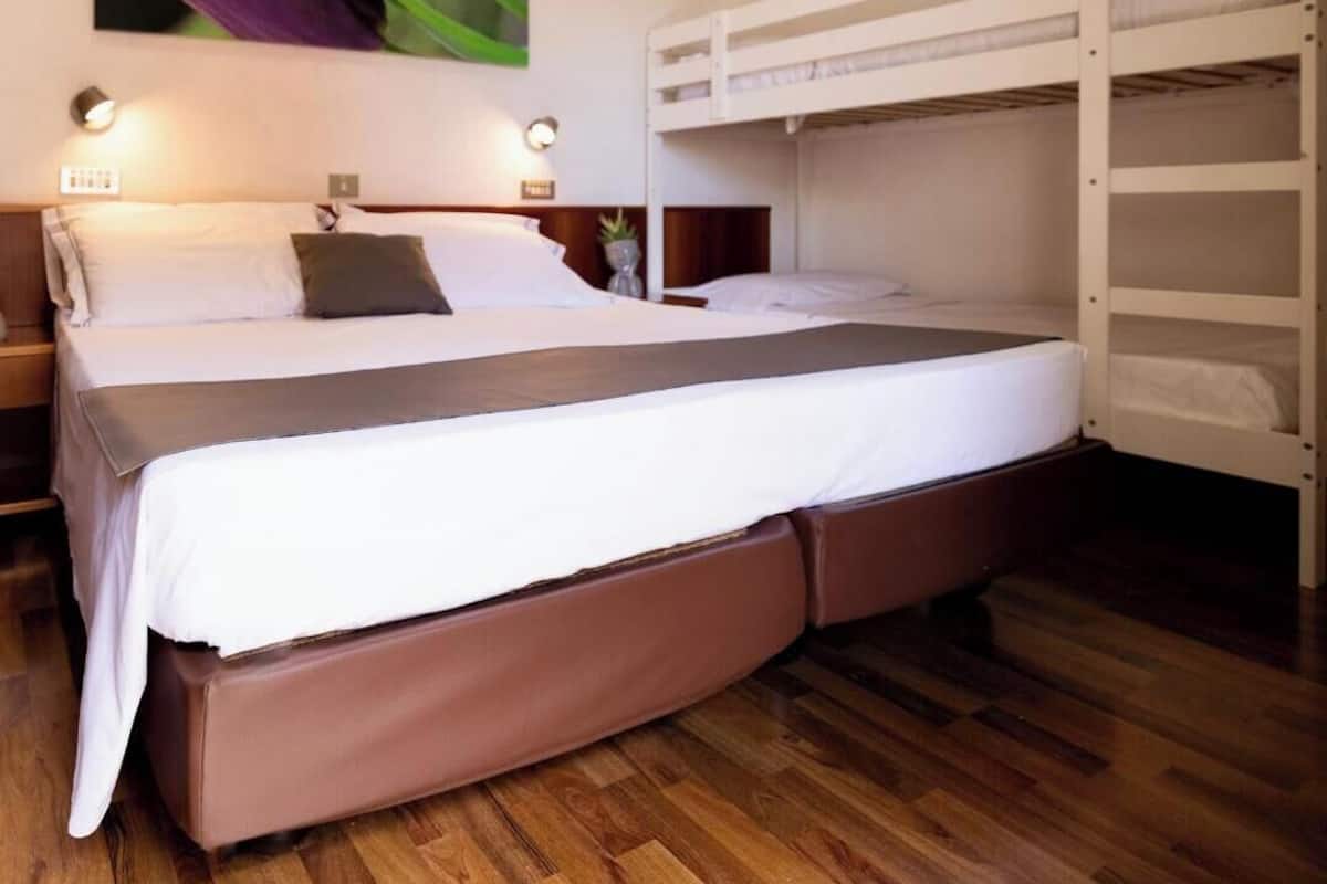 Quarto com beliche, uma cama de solteiro, abajures e piso de madeira.