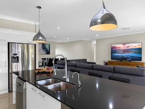 Een moderne keuken met een centraal eiland, roestvrijstalen apparatuur en hangende lampen.
