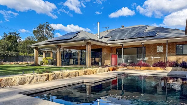 Una casa moderna con piscina, paneles solares y un porche cubierto.