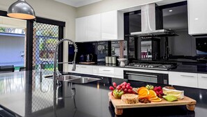 Una cocina moderna con una isla central, electrodomésticos de acero inoxidable y una selección de frutas y quesos sobre la isla.