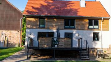 Ein zweistöckiges Haus mit rotem Ziegeldach, einer Holzterrasse und einer Steinmauer.