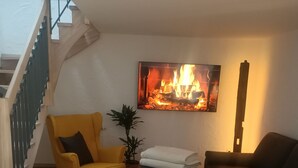 Ett vardagsrum med en trappa, en gul fåtölj, en svart soffa, en växt och en öppen spis.