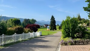 A paved road with a white fence, a brick pathway, and a grassy area with trees and flowers. - Apartment 'Wohlfühlappartement Sonnenhalde' with Private Terrace, Garden & Wi-Fi (Sigmarszell)