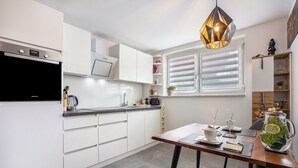 A modern kitchen with white cabinets, a built-in oven, and a dining area with a table set for two. - Apartment 'Wohlfühlappartement Sonnenhalde' with Private Terrace, Garden & Wi-Fi (Sigmarszell)