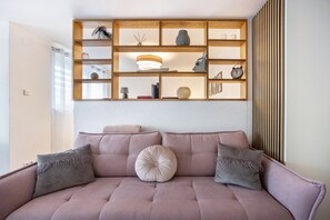 Ein Wohnzimmer mit Sofa, Kissen, einem Holzboden mit Dekoration und einer Wand mit vertikalen Jalousien.