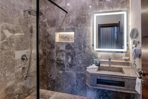 A modern bathroom with a glass-enclosed shower, a marble-tiled wall, a built-in sink, and a mirror with a light above it. - Grand hotel alhamra  (Jeddah)