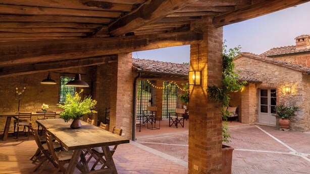 Un patio al aire libre con mesa y sillas de madera, paredes de piedra y piso de ladrillo.