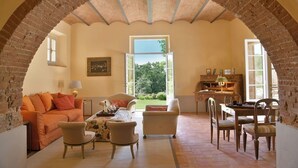 Una habitación con un arco de ladrillo, un sofá, sillas, una mesa y vistas a través de un puerta abierta.