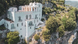 A large, white building with multiple balconies and arched windows, situated on a cliff with surrounding greenery. - Villa in Ravello with 6 bedrooms sleeps 15 (Ravello)