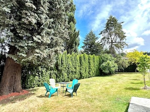Une terrasse avec deux chaises et une table, entourĂ©e dâune pelouse bien entretenue et de grands arbres.