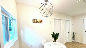 A room with a round table, chairs, a potted plant, a ceiling light fixture, and a window. - Cozy new 2-bedroom suite with AC & big private yard in charming Burnaby (Burnaby)