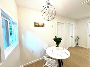 Una habitación con una mesa redonda, sillas, una planta en maceta, una lámpara del techo y una ventana.