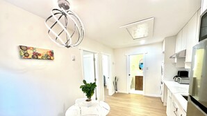 A modern kitchen with white cabinets, a stainless steel refrigerator, and a dining area with a white table and chairs. - Cozy new 2-bedroom suite with AC & big private yard in charming Burnaby (Burnaby)