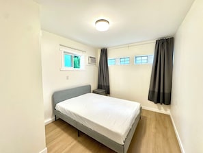 Quarto com cama, janela, ar condicionado e luminária de teto.