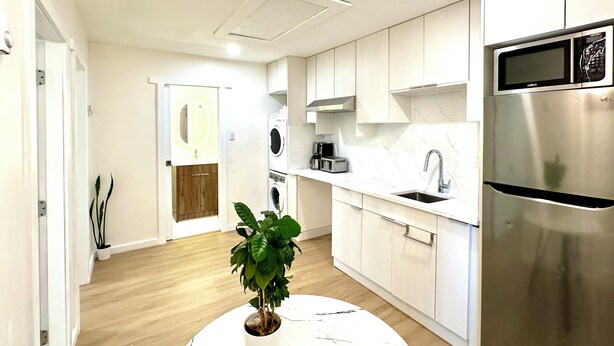 A modern kitchen with white cabinetry, a stainless steel refrigerator, a built-in oven, and a ceiling fan. - Cozy new 2-bedroom suite with AC & big private yard in charming Burnaby (Burnaby)