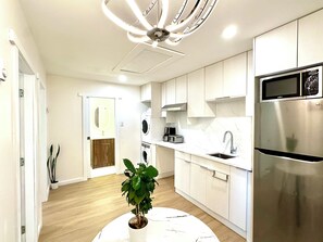 Une cuisine moderne avec des meubles blancs, un réfrigérateur en acier inoxydable, un four encastré et un ventilateur de plafond.