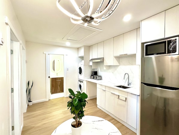 Une cuisine moderne avec des meubles blancs, un réfrigérateur en acier inoxydable, un four encastré et un ventilateur de plafond.
