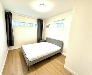Une chambre Ă coucher comprenant un lit, une table de chevet, une fenĂȘtre avec des rideaux, un appareil de climatisation et un luminaire au plafond.