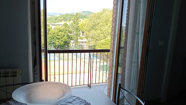 Ein Balkon mit Blick auf einen Park und Gebäude, ein Tisch mit weißer Tischdecke und ein Stuhl.