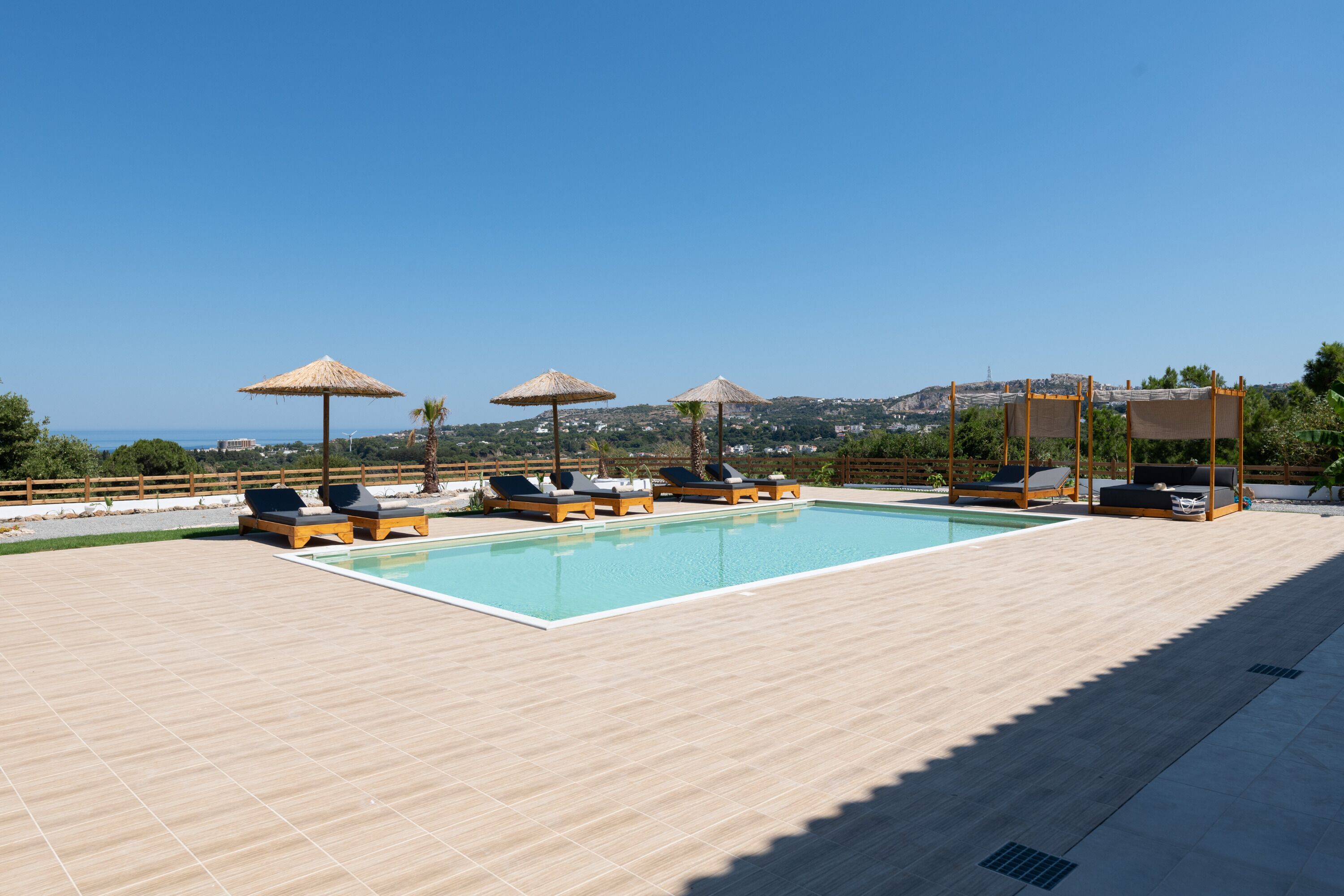 A rooftop pool with lounge chairs and umbrellas, a clear sky, and a distant view of a cityscape.
