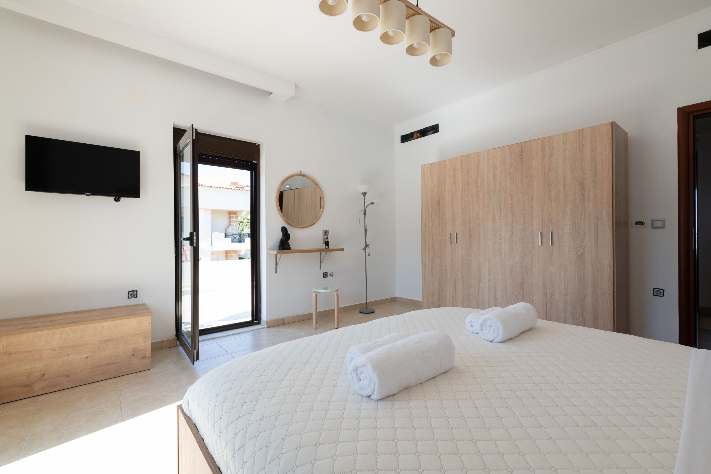 Ein Schlafzimmer mit einem Bett, einem Holzschrank, einem Fernseher und einem durch eine offene Tür einsehbaren Badezimmer.