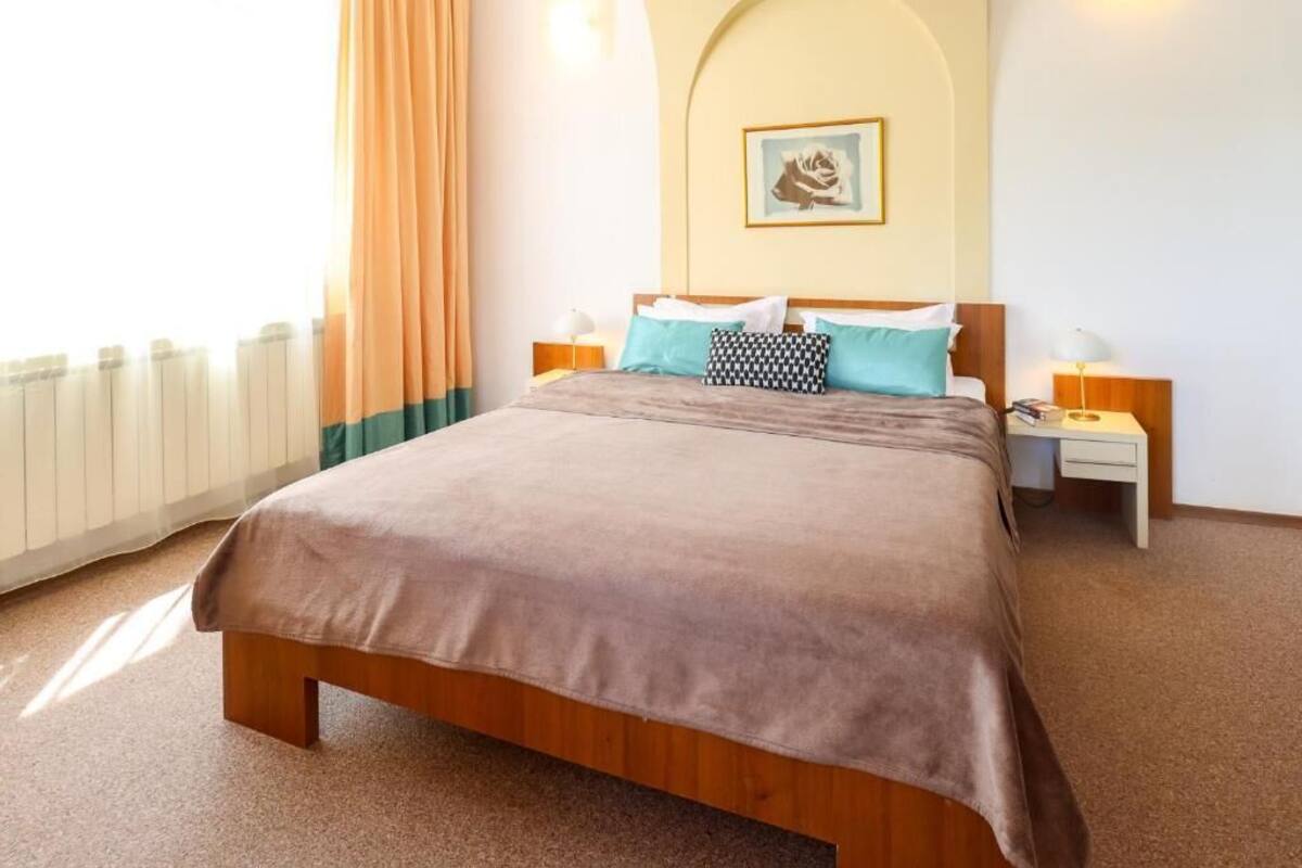 A hotel room with a large bed, two bedside tables, a nightstand, a picture on the wall, and a window with curtains.