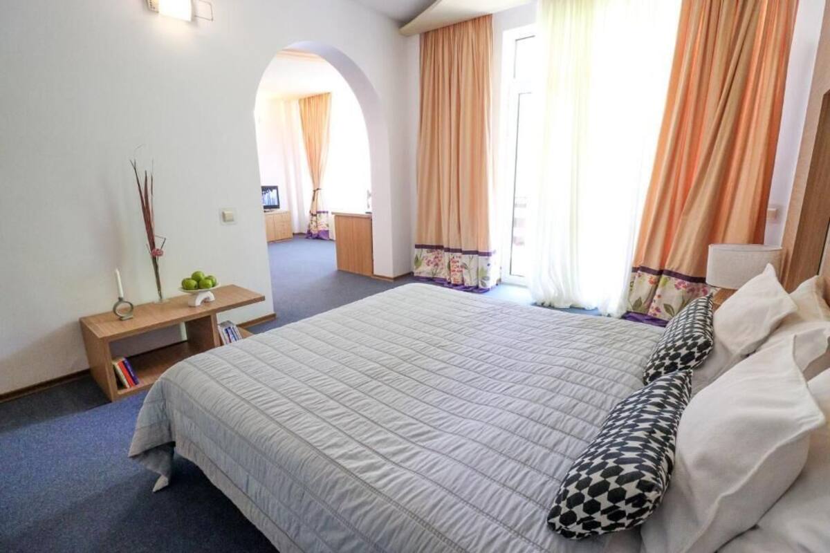 A hotel room with a large bed, a bedside table, a lamp, and a view of the hallway.