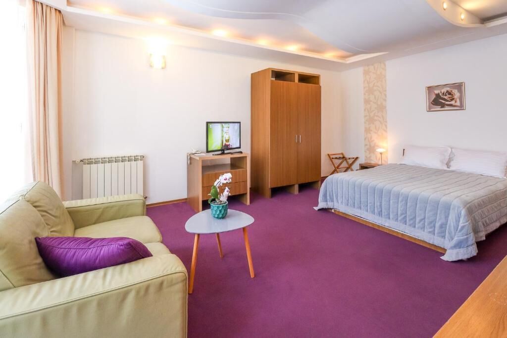 Een slaapkamer met een bed, een bank, een kleine tafel met een plant, een garderobe en een radiator.
