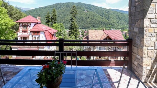 En balkon med et glasbord og stole, en potteplante og udsigt til et bjerg og huse.