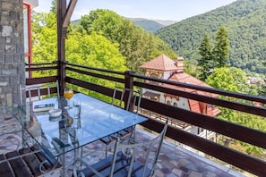 Een glazen tafel met stoelen op een balkon met uitzicht op een bergachtig landschap.