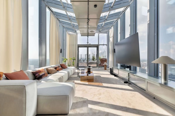 Ein modernes Wohnzimmer mit einem großen Sofa, einem Flachbildfernseher und Blick durch große Fenster.