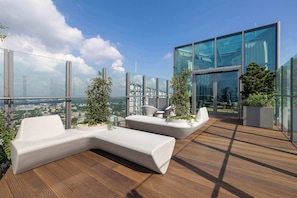 Eine Dachterrasse mit moderner Sitzgelegenheit, Glaswänden und Topfpflanzen.