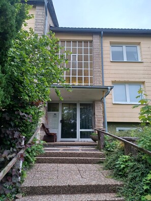 A building with a staircase leading to a door, surrounded by greenery.