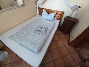 A bed with a wooden headboard, a white mattress, a quilt, and a folded towel. - Nice 30 m2 apartment in the Harz region (Braunlage)