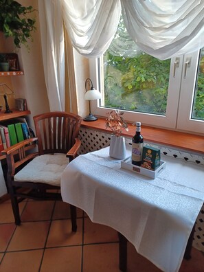 A room with a table, chair, books, a lamp, a bottle, and a box of Al Rashia coffee. - Nice 30 m2 apartment in the Harz region (Braunlage)