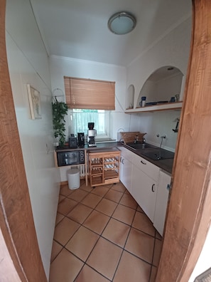 A compact kitchen with white cabinets, a microwave, a coffee maker, and a small dining area with a table and chairs. - Nice 30 m2 apartment in the Harz region (Braunlage)