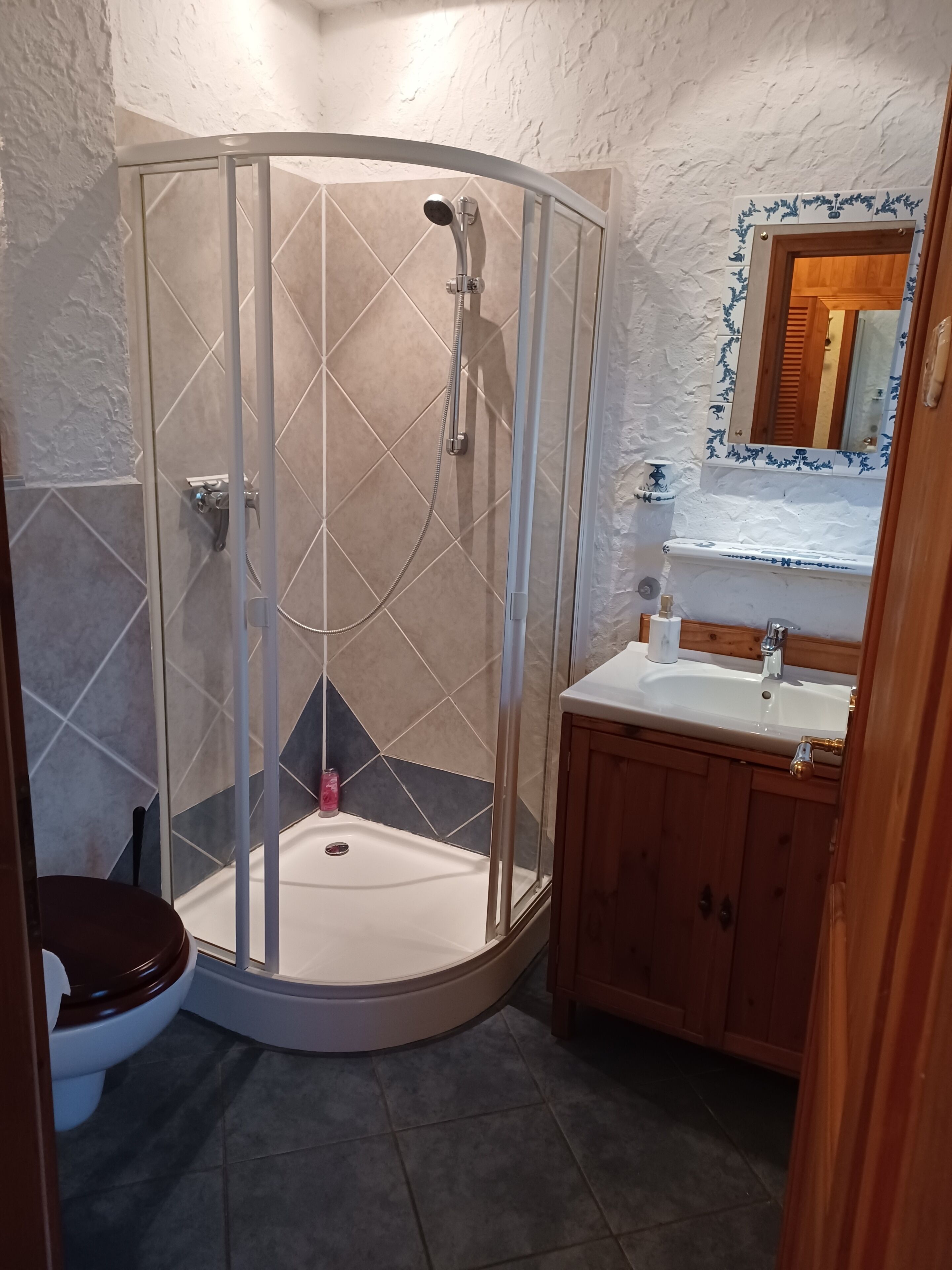 A bathroom with a glass-enclosed shower, a toilet, and a sink with wooden cabinets.