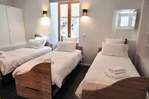 A bedroom with two beds, wooden headboards, white bedding, and a window with a view of a building.