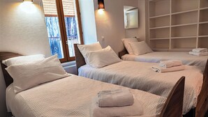 Camera d'albergo con tre letti, ognuno con copripiumino e cuscini bianchi, e un'ampia finestra vista.