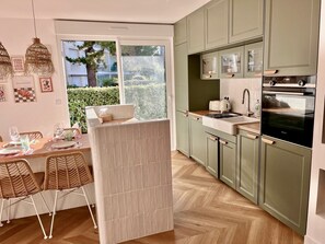 Eine moderne Küche mit grünen Schränken, einem eingebauten Backofen und einem Essbereich mit Korbstühlen.