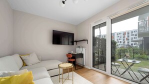 A modern living room with a sofa, a small round table, a desk with two chairs, and a large sliding glass door leading to an outdoor area. - Cozy Studio with a Garden | A Place to Work (Wrocław)