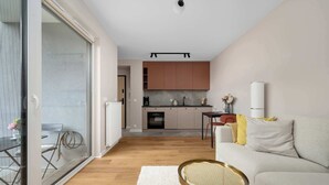 A modern apartment with a dining area, kitchen, and a living room with a sofa and a small round table. - Cozy Studio with a Garden | A Place to Work (Wrocław)