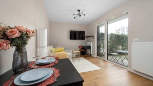 A modern living room with a dining area, a flat-screen TV, and a large sliding glass door to a balcony. - Cozy Studio with a Garden | A Place to Work (Wrocław)