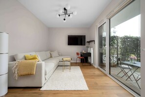 A modern living room with a sofa, a small table, a TV mounted on the wall, and a large sliding glass door leading to an outdoor area. - Cozy Studio with a Garden | A Place to Work (Wrocław)
