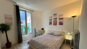 Un dormitorio con cama, una silla, un escritorio, un radiador y una ventana con cortinas.