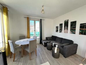 Un salon moderne avec une table à manger, un canapé gris et des œuvres d’art accrochées au mur.