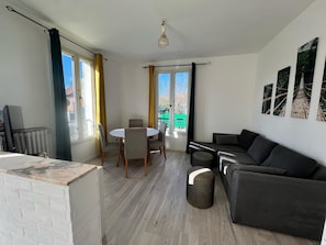 Un salon avec un canapé, une table à manger et des chaises, et une vue sur une clôture verdoyante par les fenêtres.