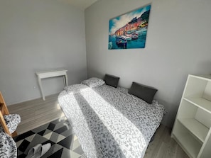 Une chambre à coucher avec un lit, une petite table, une chaise, une bibliothèque et un tableau accroché au mur.